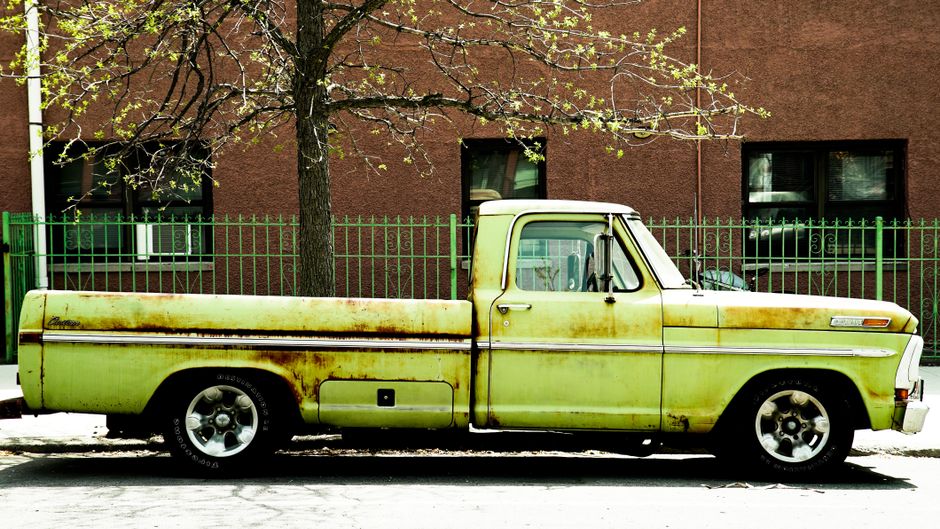 Old green pickup truck parked in front of a rustic urban building.